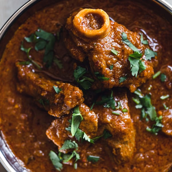 Close-up of a rich, reddish-brown Pakistani curry with bone-in meat, garnished with fresh cilantro.