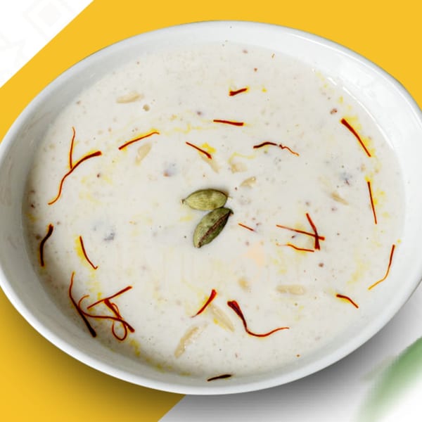 A white bowl of Pakistani kheer, garnished with saffron threads and two green cardamom pods.