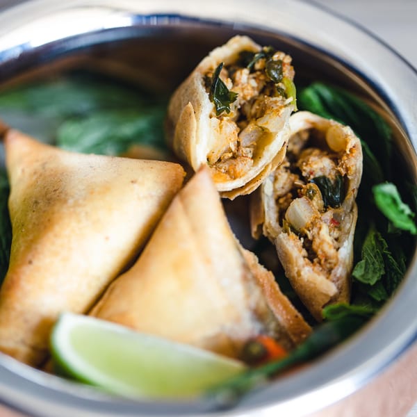 Pakistani samosas and spring rolls with lime and mint in a metal bowl.