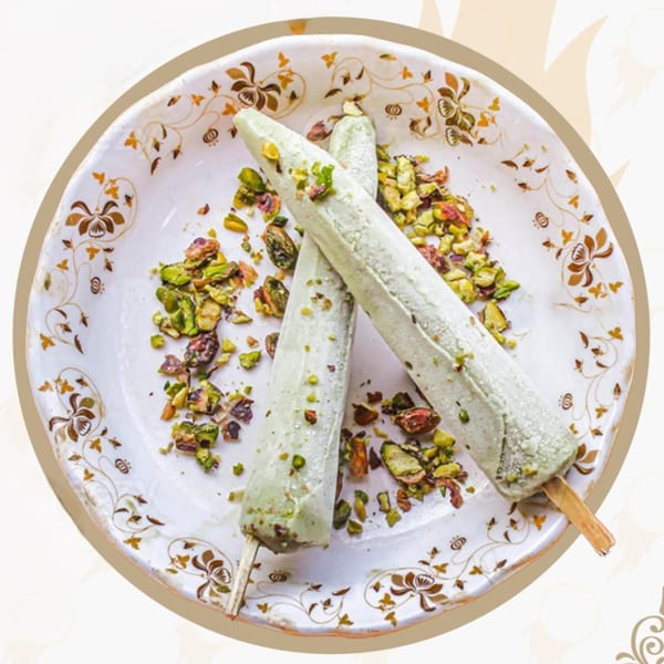 Two pistachio kulfi popsicles on a decorative white plate, sprinkled with chopped pistachios.