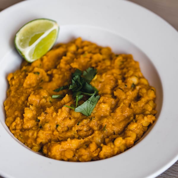 A white bowl filled with orange Pakistani dal, garnished with fresh cilantro and a lime wedge.