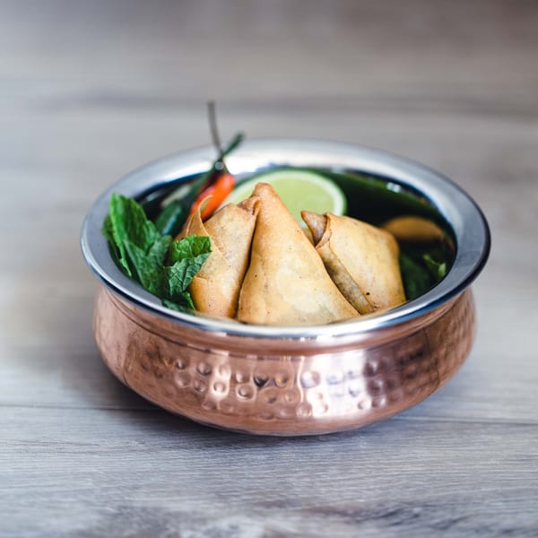 Golden-brown samosas garnished with mint, lime, and chili in a hammered copper bowl.