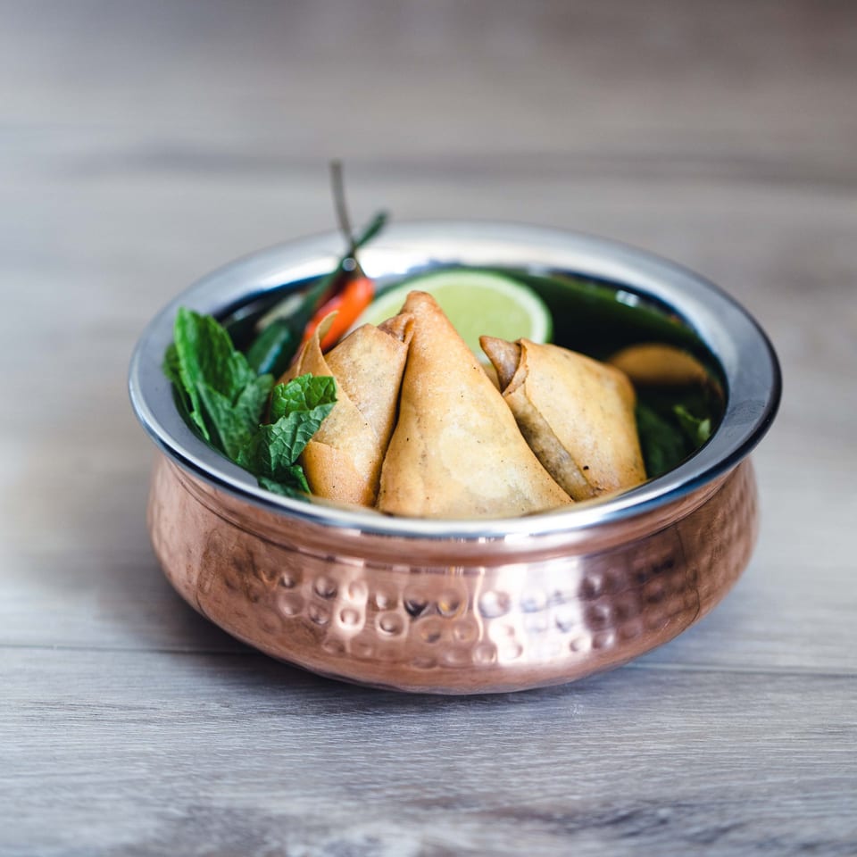 Golden-brown samosas garnished with mint, lime, and chili in a hammered copper bowl.
