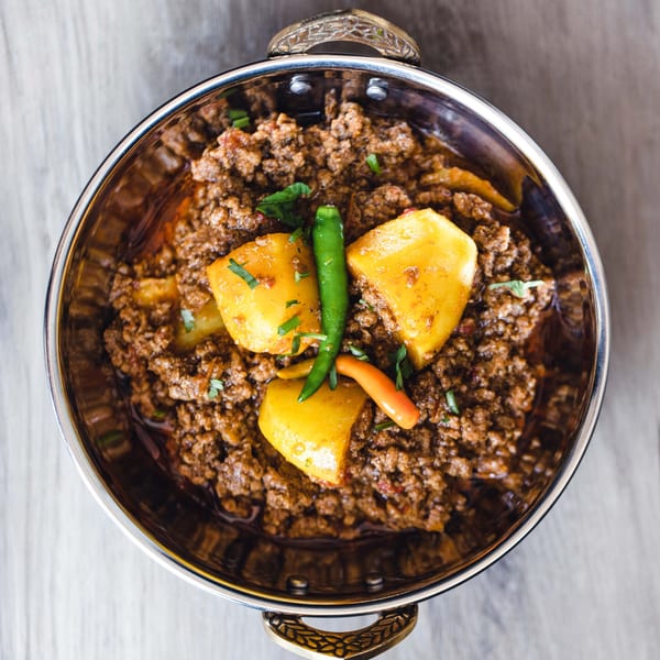 Aloo Keema, a Pakistani dish of minced meat and potatoes, garnished with green chilies in a metal bowl.