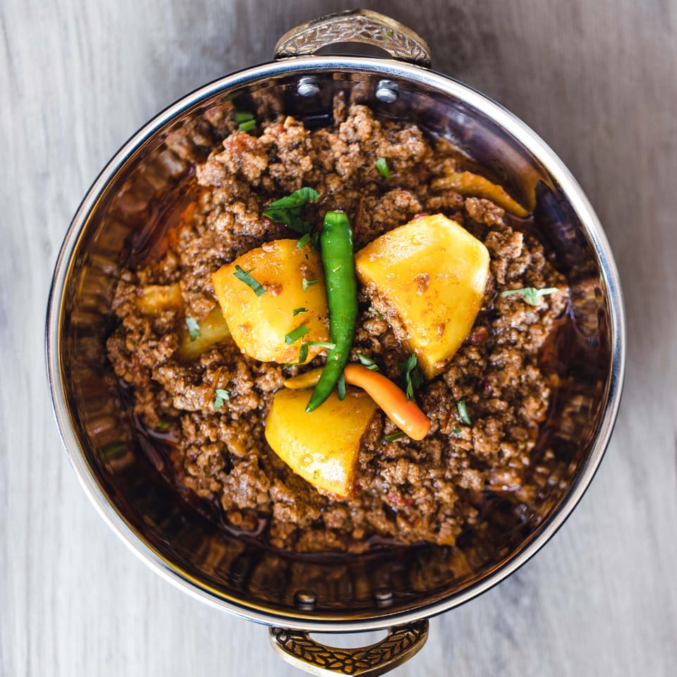 Aloo Keema, a Pakistani dish of minced meat and potatoes, garnished with green chilies in a metal bowl.