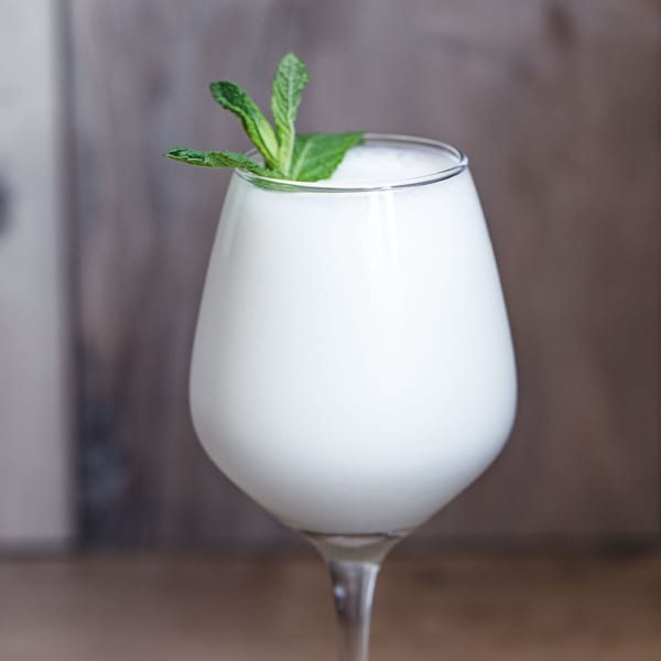 A glass of white, frothy Tandoori Restaurant lassi garnished with fresh mint leaves.