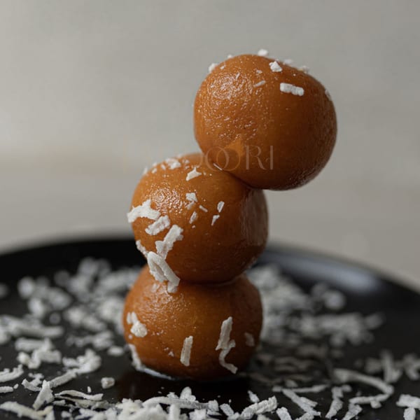 Three gulab jamun, stacked and sprinkled with coconut flakes, on a black plate.