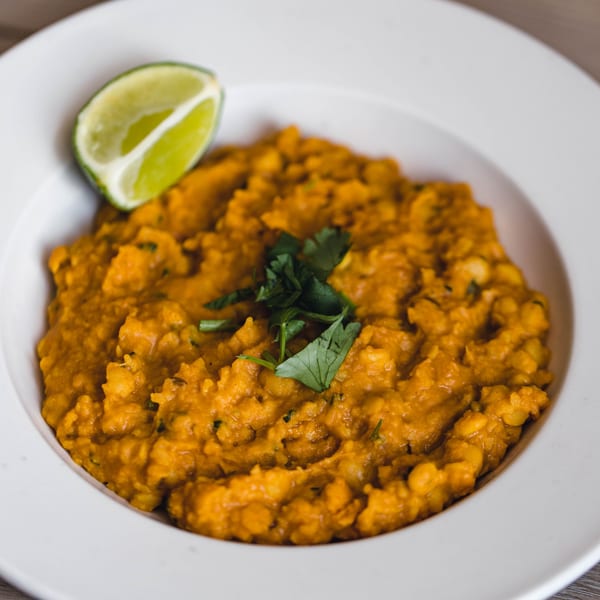A bowl of orange Pakistani dal, garnished with fresh cilantro and a lime wedge.