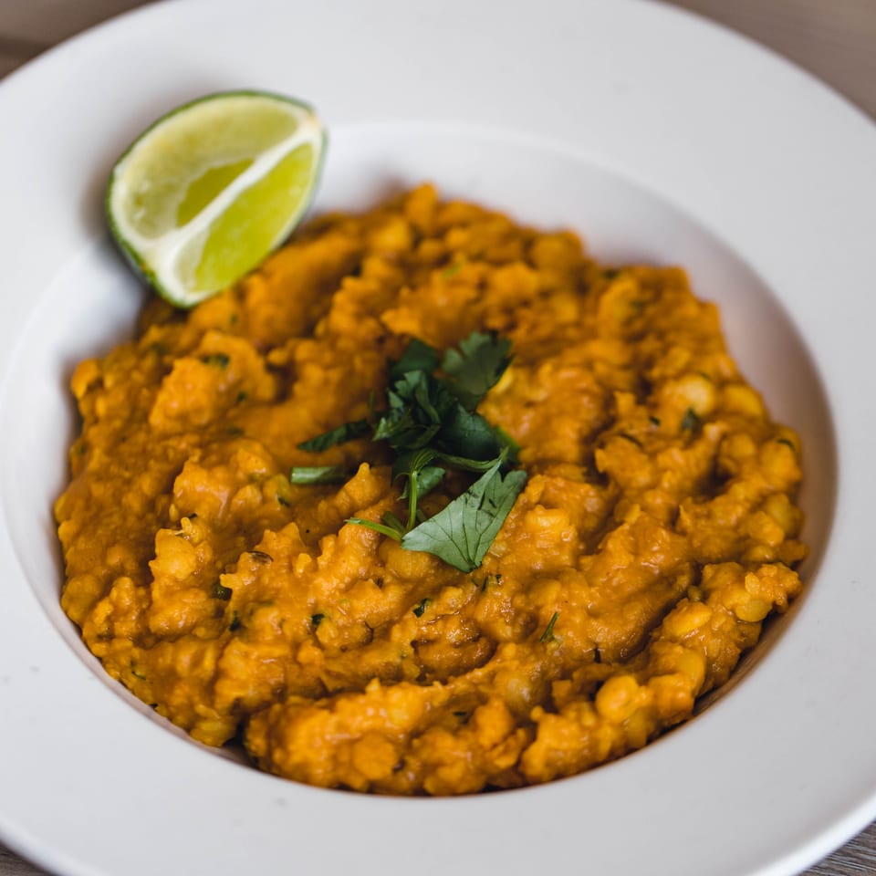 A bowl of orange Pakistani dal, garnished with fresh cilantro and a lime wedge.