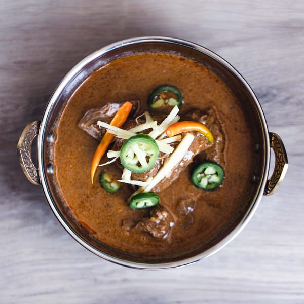 Pakistani curry in a metal bowl, garnished with sliced green chilies, ginger, and orange peppers.
